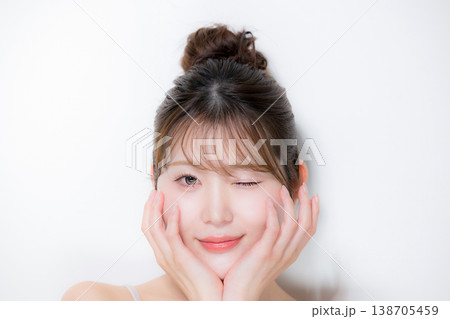 お団子のアップヘアの若い女性の艶や透明感やツヤ肌のビューティー　カメラ目線でウィンク 138705459