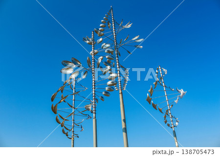 Abstract metal sculpture with swirling shapes and reflective surfaces against a clear blue sky in an outdoor setting Abstract metal sculpture with swirling shapes and reflective surfaces against a clear blue sky in an outdoor setting 138705473
