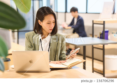 外資系IT企業のオフィスでスマホを見ながらメモを取る女性SE 138706296