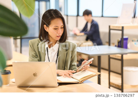 外資系IT企業のオフィスでスマホを見ながらメモを取る女性SE 外資系IT企業のオフィスでスマホを見ながらメモを取る女性SE 138706297