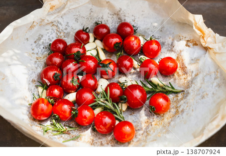 Top view of fresh cherry tomatoes garlic cloves and rosemary on baking paper. Top view of fresh cherry tomatoes garlic cloves and rosemary on baking paper. 138707924