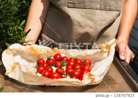 Hands holding a baking tray with fresh cherry tomatoes rosemary and garlic on parchment paper. Hands holding a baking tray with fresh cherry tomatoes rosemary and garlic on parchment paper. 138707925