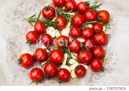 Top view of fresh cherry tomatoes garlic cloves and rosemary on baking paper. Top view of fresh cherry tomatoes garlic cloves and rosemary on baking paper. 138707929