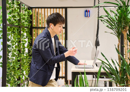 緑豊かなオフィスでスタンディングデスクを使いWeb会議をする外資系の若手男性SE 緑豊かなオフィスでスタンディングデスクを使いWeb会議をする外資系の若手男性SE 138709201