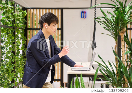 緑豊かなオフィスでスタンディングデスクを使いWeb会議をする外資系の若手男性SE 緑豊かなオフィスでスタンディングデスクを使いWeb会議をする外資系の若手男性SE 138709203