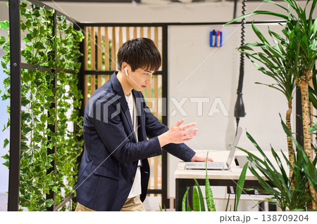 緑豊かなオフィスでスタンディングデスクを使いWeb会議をする外資系の若手男性SE 緑豊かなオフィスでスタンディングデスクを使いWeb会議をする外資系の若手男性SE 138709204