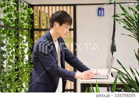 緑豊かなオフィスでスタンディングデスクを使いWeb会議をする外資系の若手男性SE 緑豊かなオフィスでスタンディングデスクを使いWeb会議をする外資系の若手男性SE 138709205
