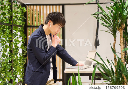 緑豊かなオフィスでスタンディングデスクを使いWeb会議をする外資系の若手男性SE 緑豊かなオフィスでスタンディングデスクを使いWeb会議をする外資系の若手男性SE 138709208