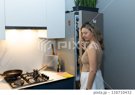 Woman opening refrigerator door in modern kitchen. Morning breakfast routine checking for fresh food. Home cooking preparation and healthy eating concept in daily life. Woman opening refrigerator door in modern kitchen. Morning breakfast routine checking for fresh food. Home cooking preparation and healthy eating concept in daily life. 138710432
