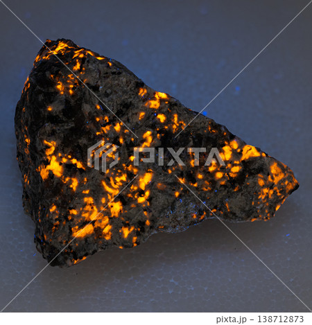 Glowing Sodalite Syenite Rock with Vibrant Orange Fluorescent Mineral Veins on Dark Textured Surface Glowing Sodalite Syenite Rock with Vibrant Orange Fluorescent Mineral Veins on Dark Textured Surface 138712873