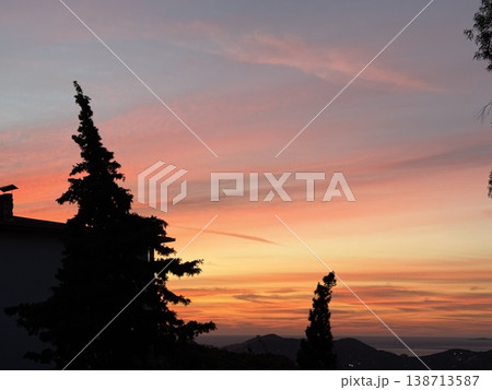 Sunset sky with silhouetted trees and distant hills, creating a serene and colorful background 138713587