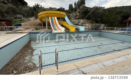 Abandoned outdoor swimming pool with empty water slides and overgrown surroundings 138713599