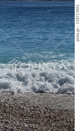 Ocean waves gently rolling onto pebble beach under clear blue sky, suitable for background use 138713601