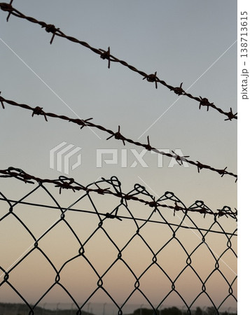 Barbed wire and fence silhouetted against a soft gradient sky background at sunset Barbed wire and fence silhouetted against a soft gradient sky background at sunset 138713615