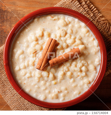 Mungunza, or traditional Brazilian creamy canjica, served in a ceramic dish with cinnamon sticks on a wooden table covered with burlap 138714004