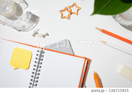 Open notebook with a speech bubble sticky note, orange pen, and star-shaped paper clips on a white desk. Copyspace Open notebook with a speech bubble sticky note, orange pen, and star-shaped paper clips on a white desk. Copyspace 138715925