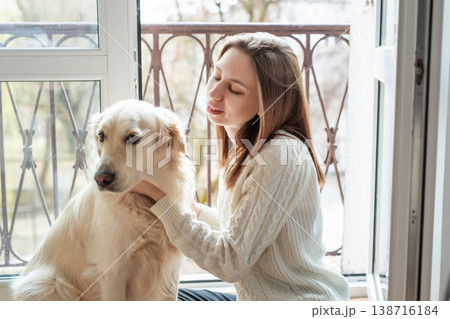 Young woman petting golden retriever dog by balcony 138716184