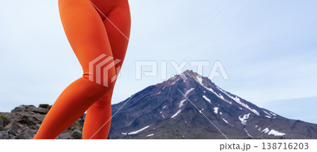 Low-angle view of a woman's legs in vibrant orange ribbed leggings white sneakers. Athlete standing on rugged rocks, perfect for active lifestyle, fitness, outdoor fashion concepts. Bright colors pop 138716203