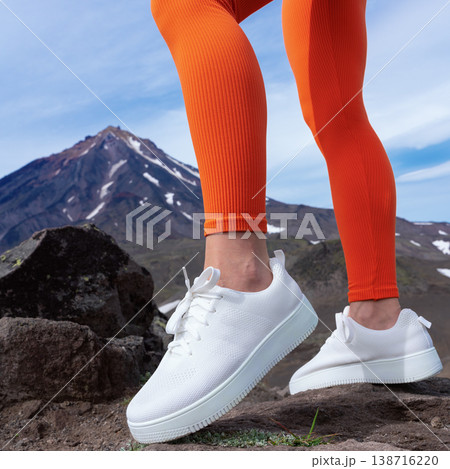 Close-up of a woman's legs in bright orange leggings and white sneakers on a rocky trail. A snow-capped mountain is in the background under a blue sky. Energetic, active lifestyle concept Close-up of a woman's legs in bright orange leggings and white sneakers on a rocky trail. A snow-capped mountain is in the background under a blue sky. Energetic, active lifestyle concept 138716220