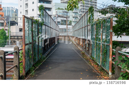 日暮里・鶯谷間の線路沿いの跨線橋 錆びたフェンス越しに望む都心の街並みと通過する鉄道 138716598