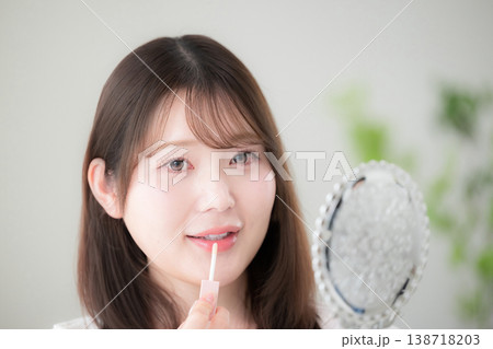 手鏡を見ながらリップを塗る女性のナチュラルメイクと美容ケア　リップグロスや唇のケアなど 138718203
