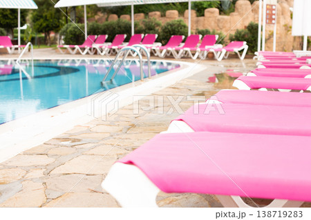 A row of pink deck chairs standing near hotel swimming pool. 138719283