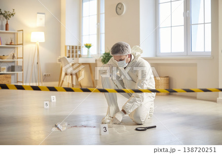 Forensic investigator in protective suit examining evidences near marked spots at crime scene. Forensic investigator in protective suit examining evidences near marked spots at crime scene. 138720251
