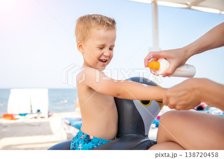 Mother applying sunscreen protection creme on cute little baby boy kid hand. Mum using sunblocking lotion to protect baby from sun during summer sea vacation. Child healthcare travel vacation time 138720458