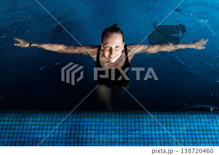 Above top view portrait of young adult caucasian female model in sport black swimsuit stand in clear blue water of indoor swimming pool at dark evening time. Relax harmony and wellness spa therapy 138720460