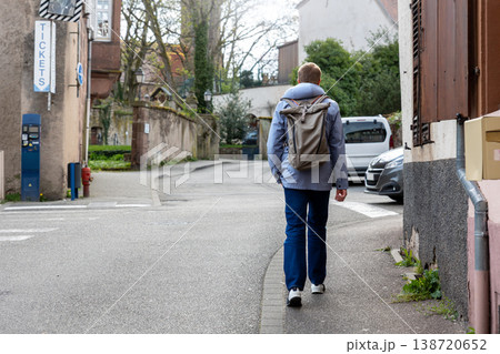 Man wear backpack walking along quiet European street traveler exploring town during daytime journey. Urban travel scene pedestrian perspective casual lifestyle tourism atmosphere sense of discovery Man wear backpack walking along quiet European street traveler exploring town during daytime journey. Urban travel scene pedestrian perspective casual lifestyle tourism atmosphere sense of discovery 138720652