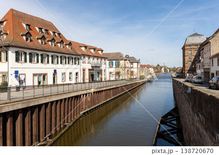 Saverne canal Alsace historic architecture dormer roofs stone embankment calm waterway under blue sky. Scenic European townscape waterfront street travel destination tranquil urban panorama 138720670
