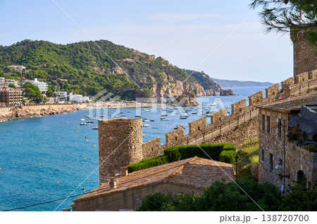 A picturesque view of Tossa de Mar, featuring the ancient castle walls overlooking a tranquil bay filled with boats on a clear day. A picturesque view of Tossa de Mar, featuring the ancient castle walls overlooking a tranquil bay filled with boats on a clear day. 138720700