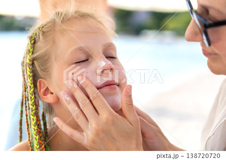 Mother applying sunscreen child face nose sunny hot beach day sea summer vacation. Caring moment parenting skin protection candid family safety. Childhood wellbeing outdoor holiday lifestyle seaside 138720720