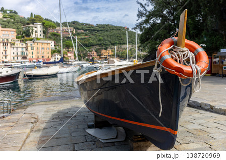 Classic wooden boat displayed near a picturesque harbor with sailboats and hillside buildings in the background. Classic wooden boat displayed near a picturesque harbor with sailboats and hillside buildings in the background. 138720969