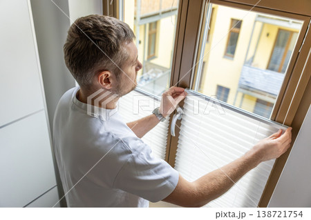 Man installing pleated blinds on window at home interior with natural daylight Man installing pleated blinds on window at home interior with natural daylight 138721754
