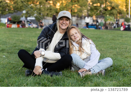 Happy Mother And Daughter Sitting On Green Grass In Park During Golden Hour Happy Mother And Daughter Sitting On Green Grass In Park During Golden Hour 138721789
