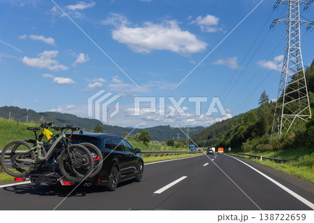 Car bicycles on rear carrier driving along mountain highway forest valley blue sky clouds sunny day. Summer road trip scene travel cycling adventure transport mobility countryside tourism Car bicycles on rear carrier driving along mountain highway forest valley blue sky clouds sunny day. Summer road trip scene travel cycling adventure transport mobility countryside tourism 138722659