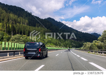 Luxury black minivan driving along alpine highway between green mountains blue sky. Comfort vip van transfer transportation passenger service, Airport shuttle taxi European mountain resorts 138722670