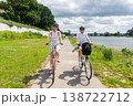 Women riding bicycles along riverside path during summer day with green park landscape and cloudy sky. Active lifestyle, friendship, outdoor recreation healthy activity travel freedom leisure cycling 138722712
