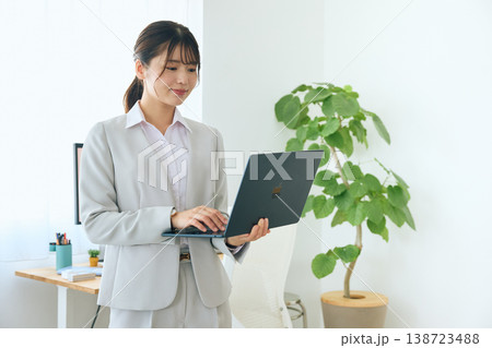 ノートパソコンを操作する若い女性ビジネスパーソン・オフィスで立って作業する会社員 ノートパソコンを操作する若い女性ビジネスパーソン・オフィスで立って作業する会社員 138723488