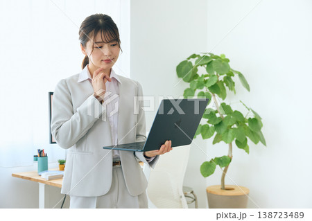 ノートパソコンを操作する若い女性ビジネスパーソン・オフィスで立って作業する会社員 ノートパソコンを操作する若い女性ビジネスパーソン・オフィスで立って作業する会社員 138723489