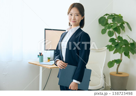 オフィスでファイルを持って立つスーツ姿の若い女性ビジネスパーソン・笑顔の会社員ポートレート 138723498