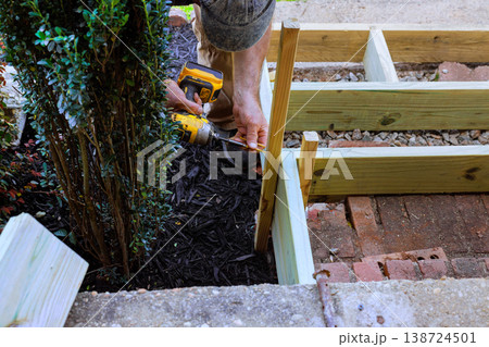 Man works with tools to build wooden steps frame around plants 138724501