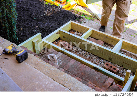 Worker builds wooden frame on pathway in garden near brick walkway Worker builds wooden frame on pathway in garden near brick walkway 138724504