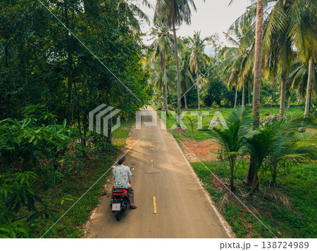 Traveler riding a scooter on a quiet road through a tropical palm forest. Traveler riding a scooter on a quiet road through a tropical palm forest. 138724989
