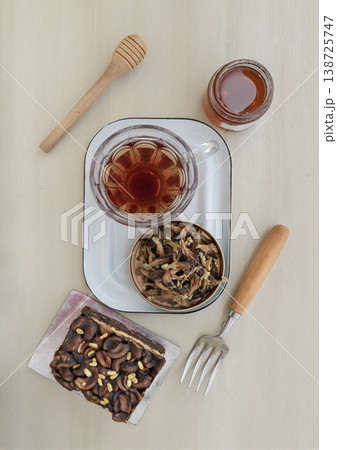 Enjoy a relaxing tea break with a rich toffee cheesecake garnished with cashews and chocolate almonds. It is served alongside butterfly pea flower tea and a jar of honey with a traditional wooden 138725747