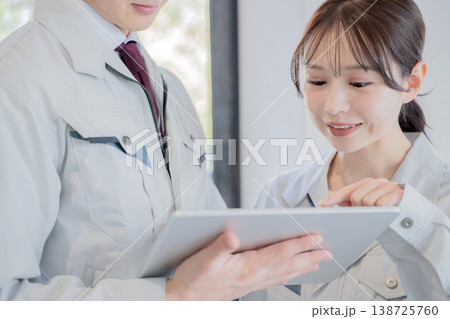 タブレットを見ながら打ち合わせをする作業着の男性と女性 138725760