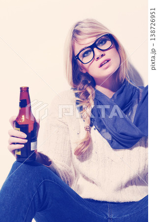 Portrait, fashion and drinking beer with a woman in studio on a white wall background to relax. Glasses, scarf and glass bottle with a beverage in the hand of a young person for winter celebration 138726951