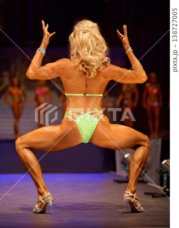 Bodybuilder, competition and woman in a bikini on the stage flexing in performance of fitness. Back, legs and female athlete winner with strong, muscle and perfect shape from training and exercise 138727005