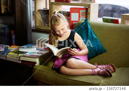 Child, girl on sofa and reading book for happy learning, education and funny story with knowledge or creative mind. Kid relax on couch with literature, English story and library in home living room 138727148